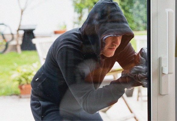 Burglar wearing a hoodie breaking into a side door of a house