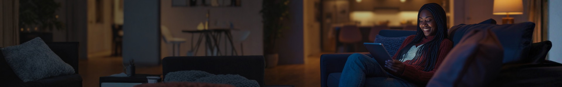 A homeowner relaxing on the couch using a tablet to control smart home lighting and security settings via the Guardian Alarm app.