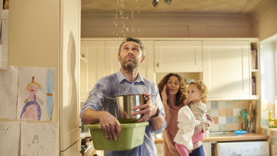 family looking at leaking ceiling with a pot ready to catch water